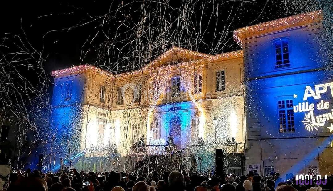 Foule rassemblée devant un bâtiment illuminé, avec des projections lumineuses et des confettis dans l'air.