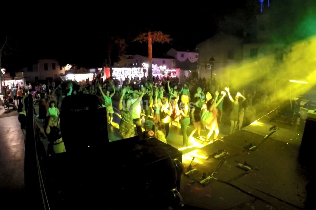 Foule dansant devant une scène éclairée par des projecteurs jaunes lors d'un concert en plein air de nuit.