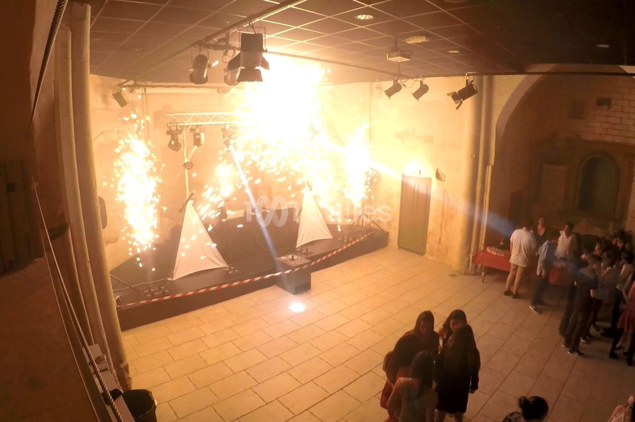 Effets pyrotechniques sur une scène dans une salle en pierre, avec un groupe de personnes rassemblées à droite.