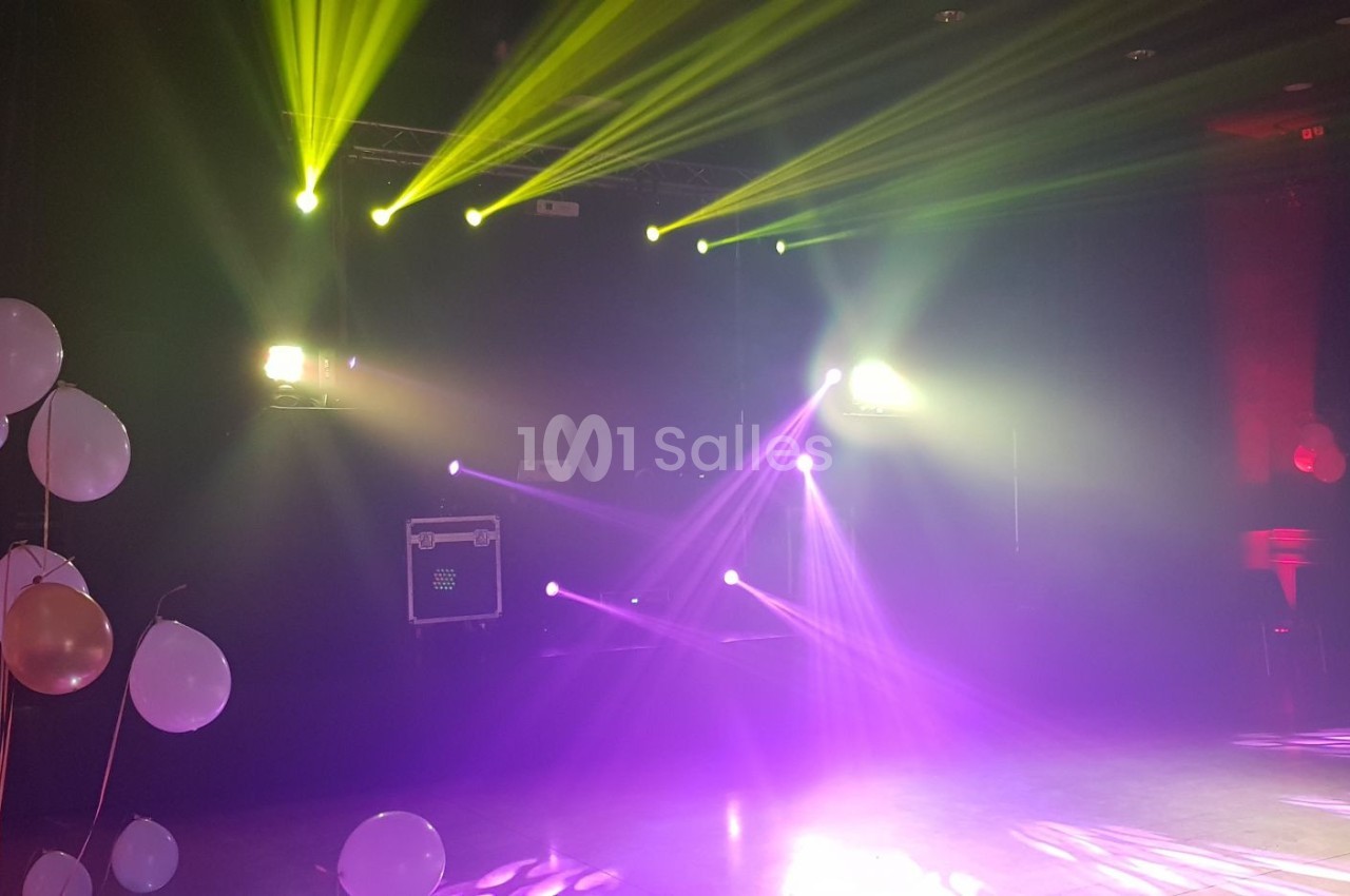 Jeux de lumières colorées dans une salle sombre décorée de ballons blancs et roses.