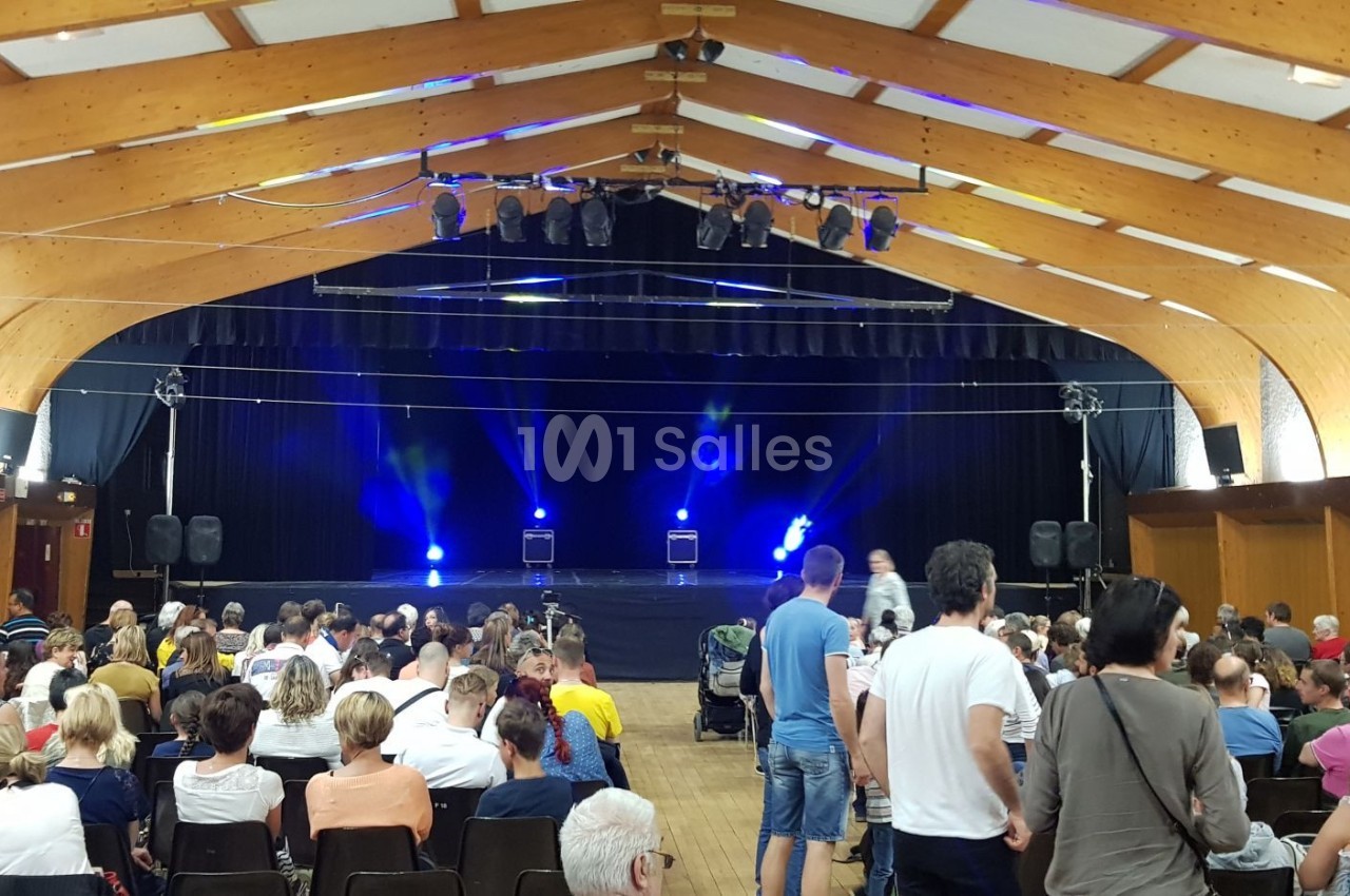 Salle de spectacle avec un public assis face à une scène éclairée par des projecteurs bleus.