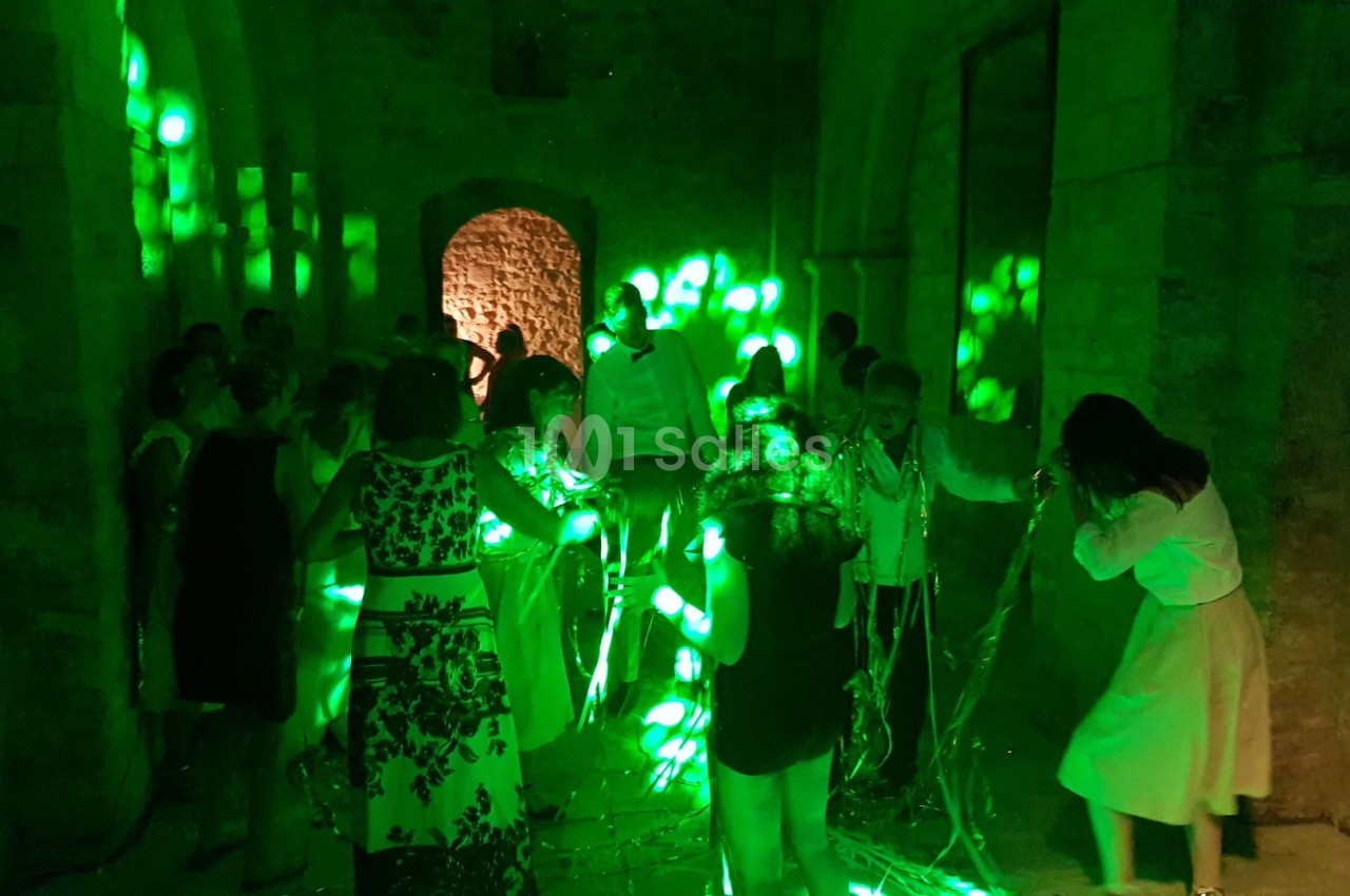 Des personnes dans une salle en pierre éclairée par des lumières vertes, certaines interagissant avec des fils lumineux.