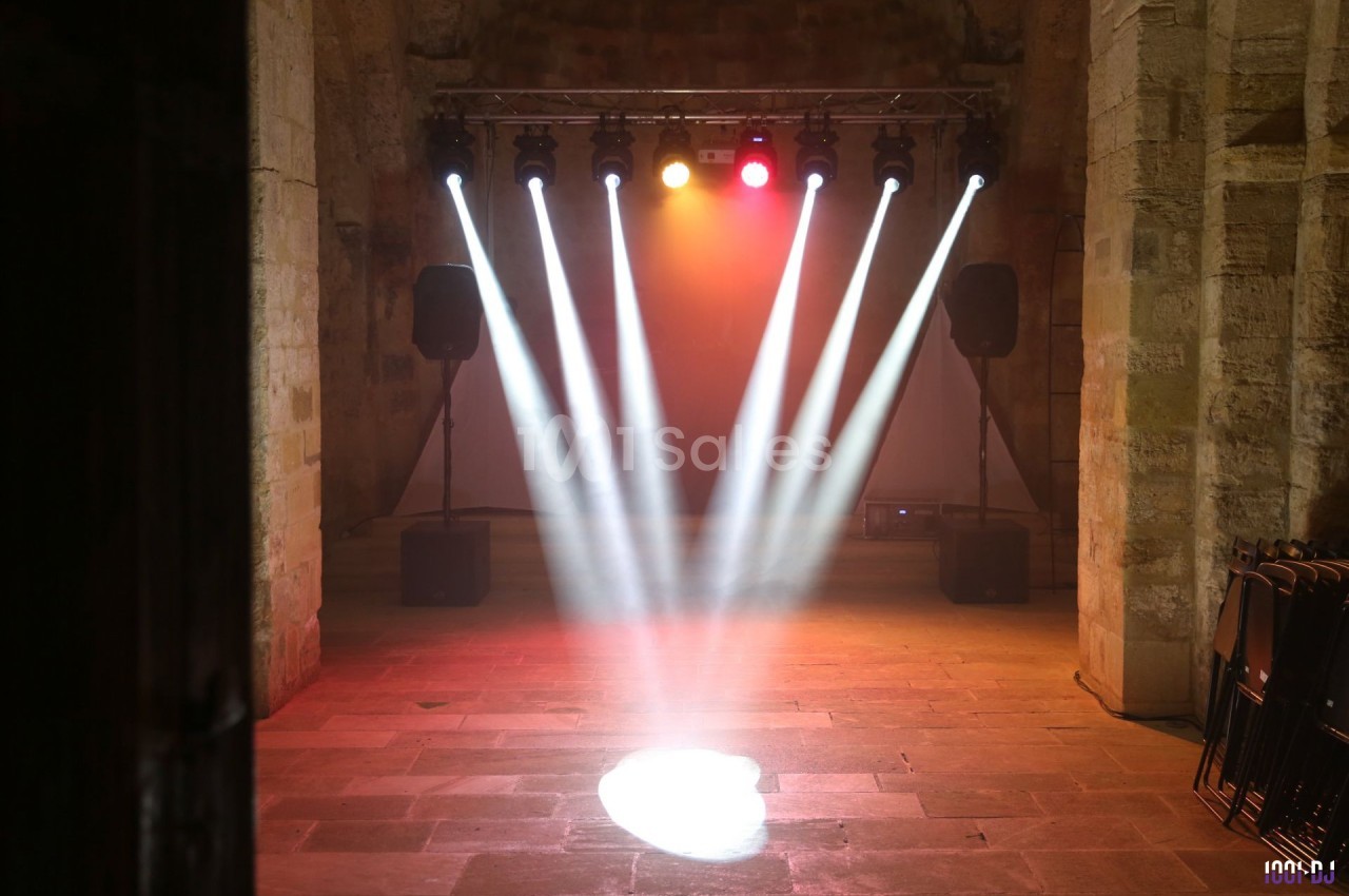 Projecteurs lumineux éclairant une scène vide dans une salle en pierre avec des murs anciens et des enceintes.