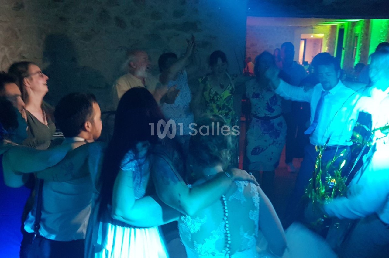 Des personnes dansent et s'enlacent dans une ambiance festive avec des lumières colorées dans une salle en pierre.