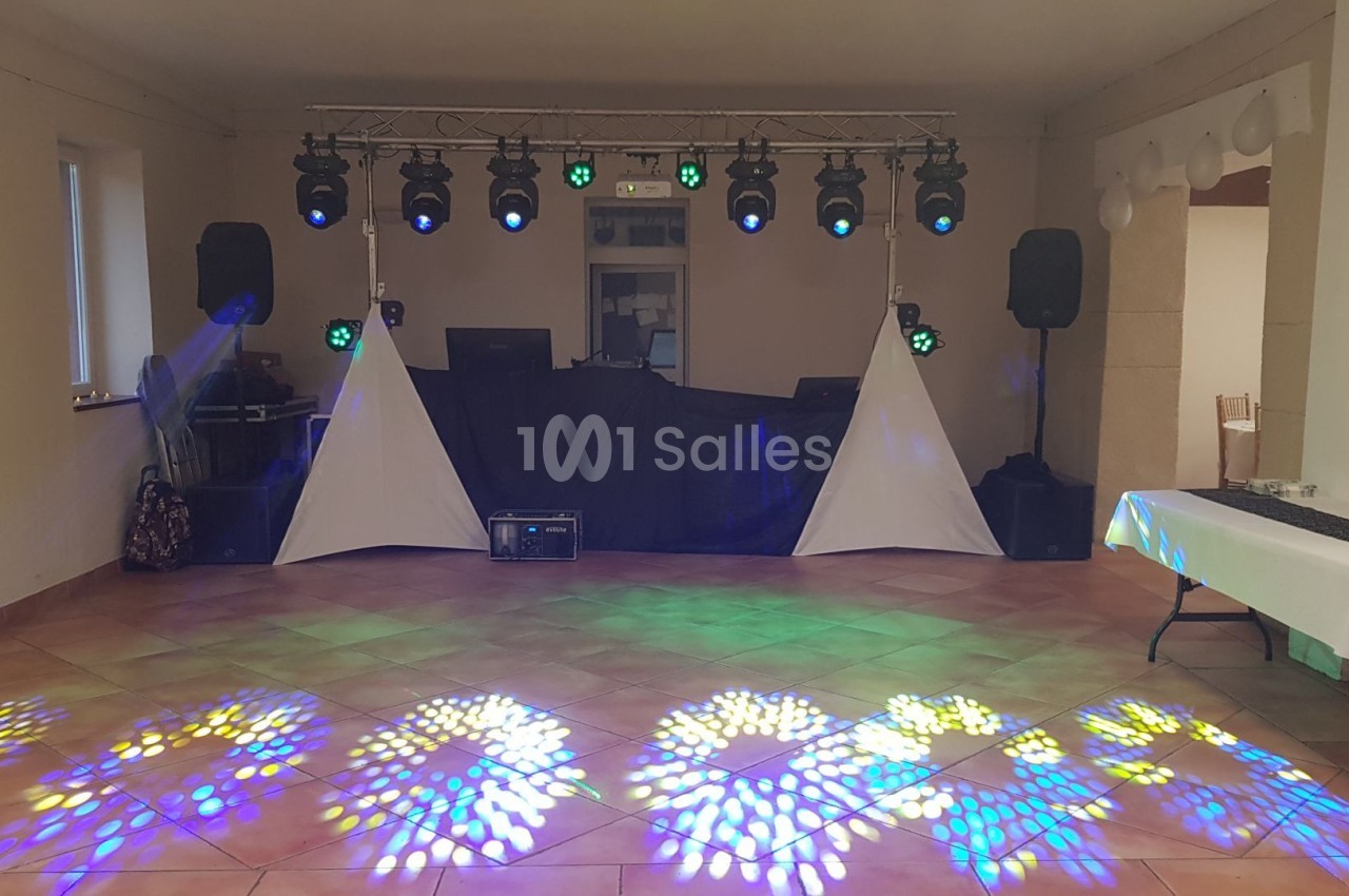 Salle avec éclairage de scène coloré, piste de danse illuminée, tables sur les côtés et matériel audio en arrière-plan.
