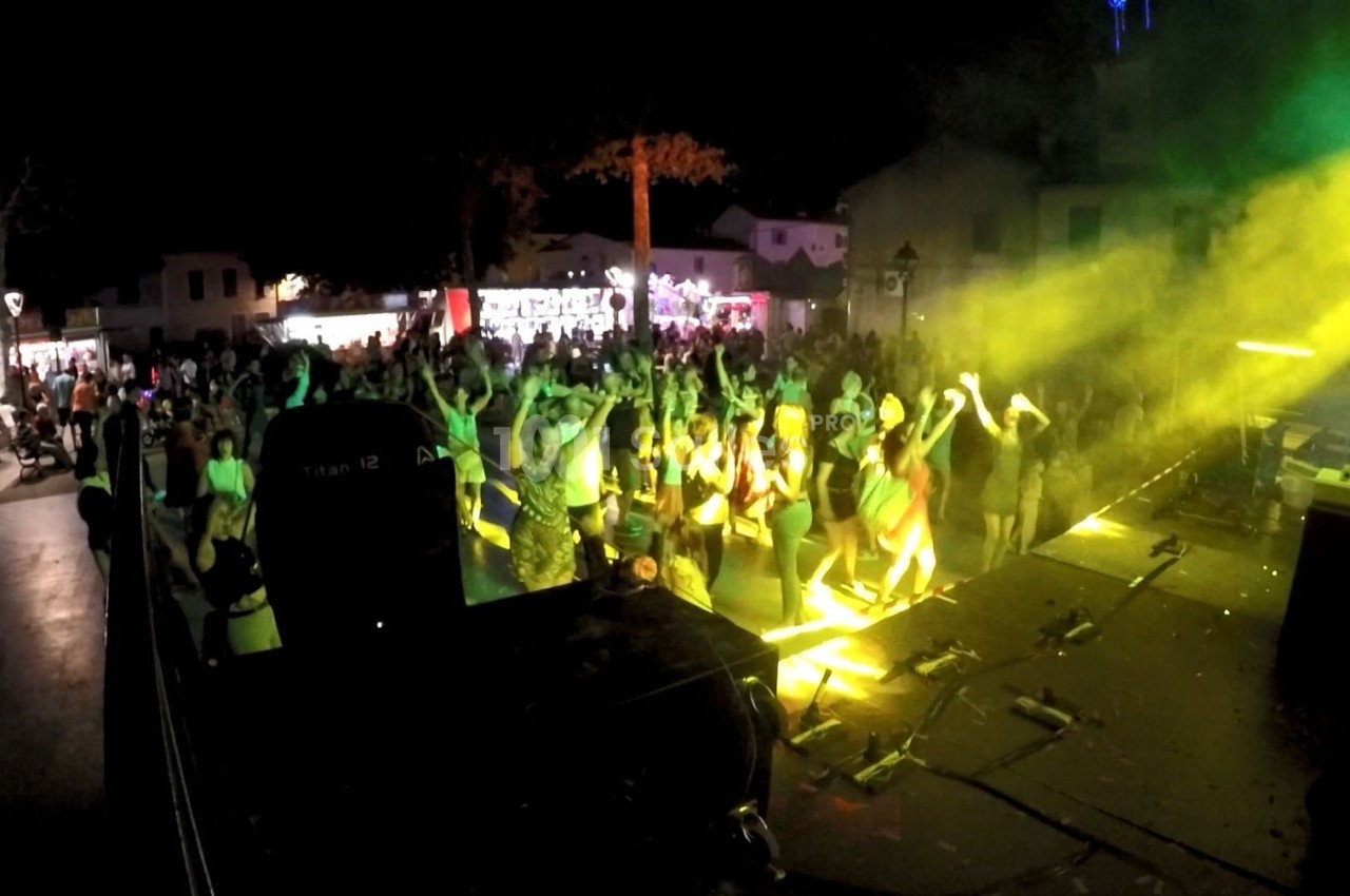 Foule dansant devant une scène éclairée par des projecteurs jaunes lors d'un concert en plein air de nuit.