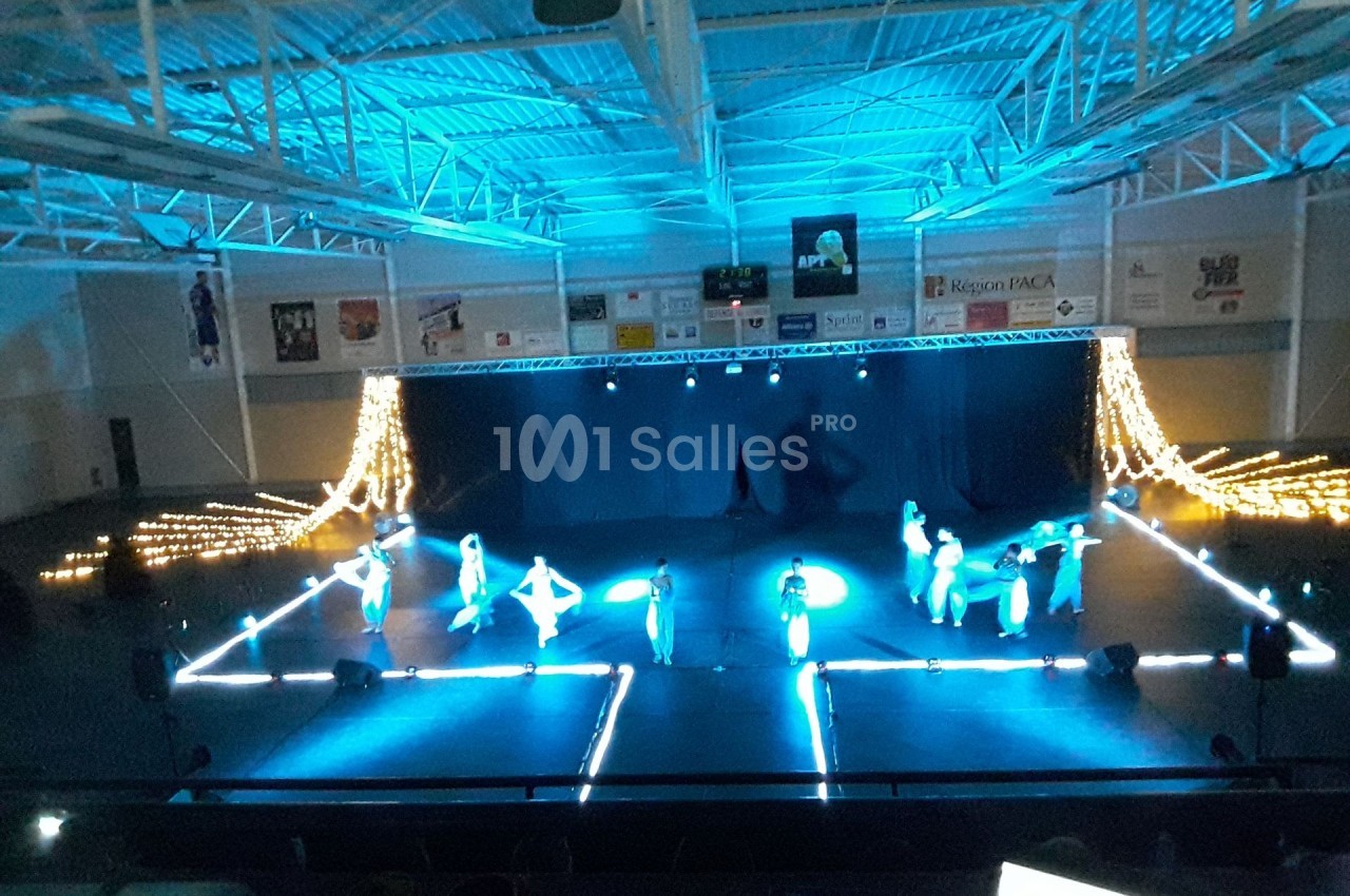 Des danseurs sur une scène éclairée en bleu dans une salle de spectacle avec des guirlandes lumineuses en arrière-plan.