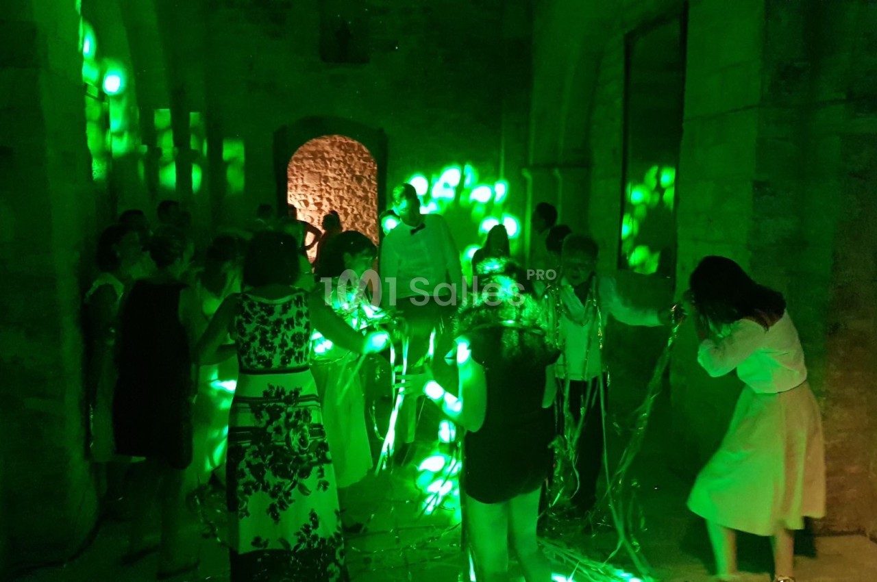 Des personnes dans une salle en pierre éclairée par des lumières vertes, certaines interagissant avec des fils lumineux.