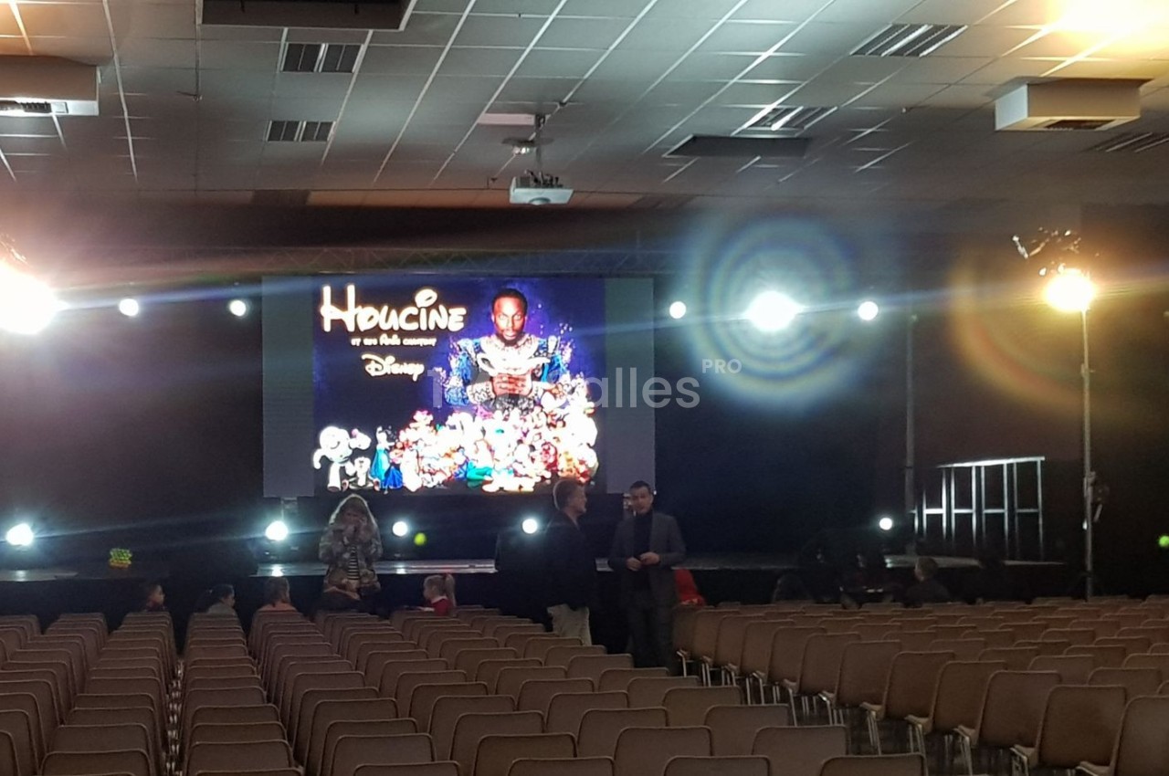 Salle de conférence vide avec un écran géant affichant une affiche de film et des projecteurs allumés.
