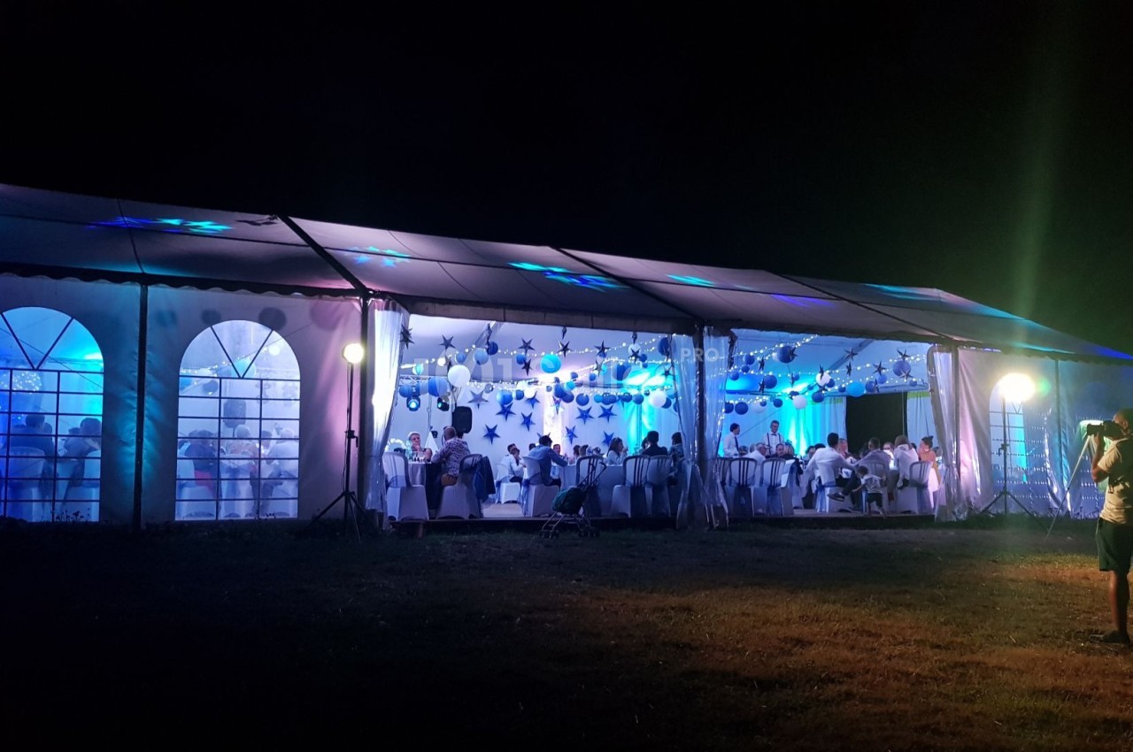 Grande tente éclairée en soirée, décorée de guirlandes lumineuses, accueillant des invités assis à des tables.