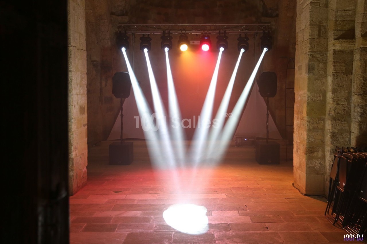 Projecteurs lumineux éclairant une scène vide dans une salle en pierre avec des murs anciens et des enceintes.