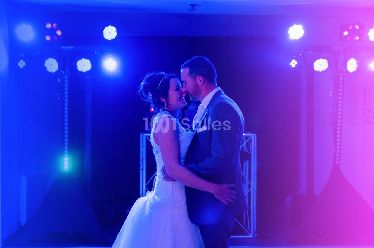 Un couple en tenue de mariage danse sous des lumières colorées dans une ambiance festive.