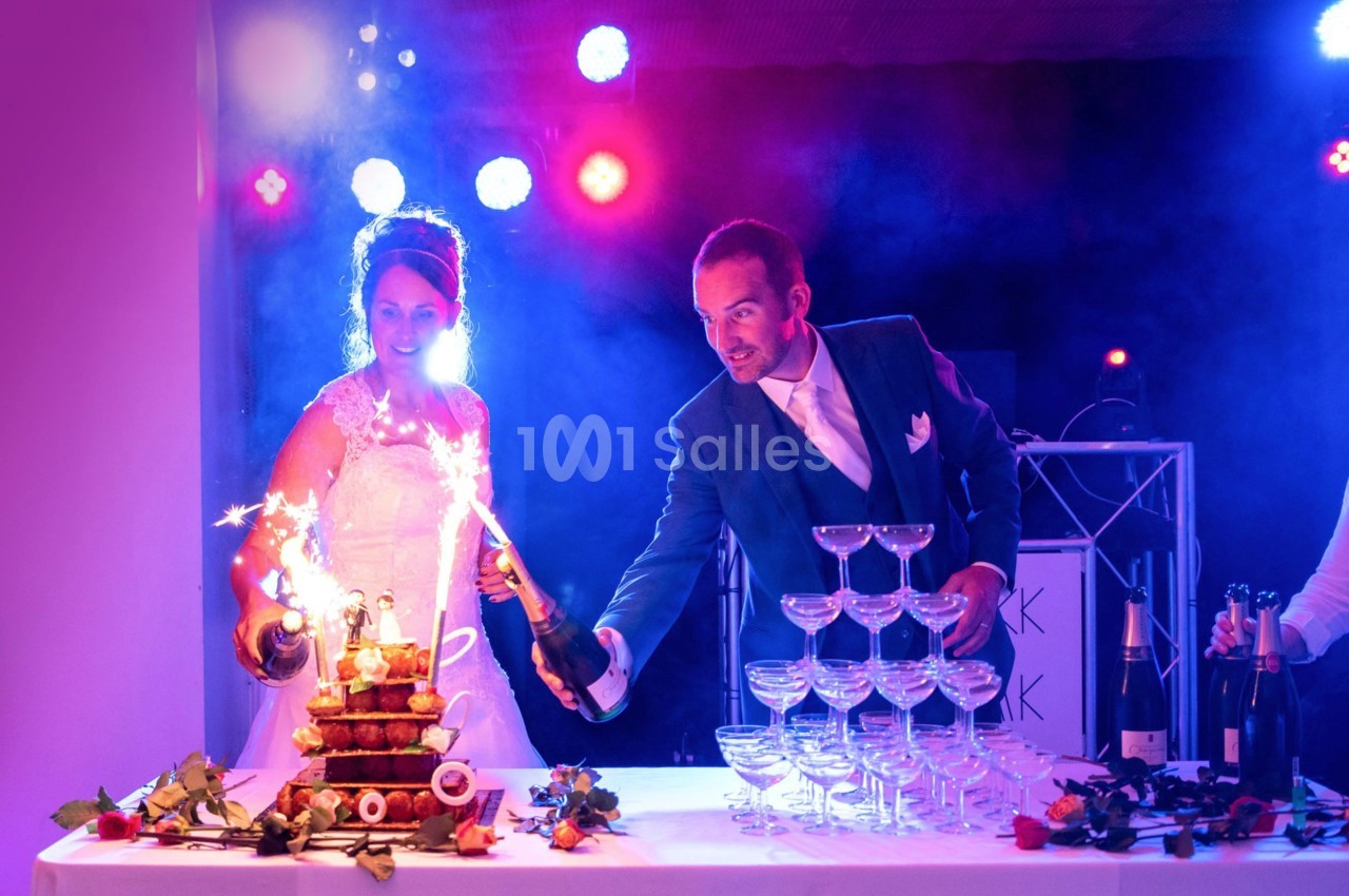 Un couple en tenue de mariage verse du champagne sur une pyramide de verres illuminée par des étincelles.