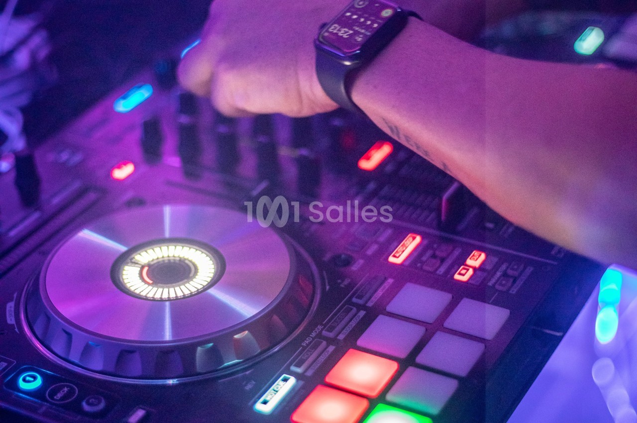 Main ajustant les commandes d'une table de mixage lumineuse dans une ambiance colorée.