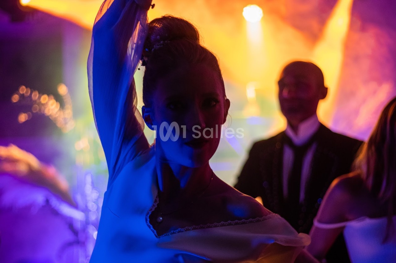 Femme dansant sous des lumières colorées, entourée de silhouettes floues dans une ambiance festive.