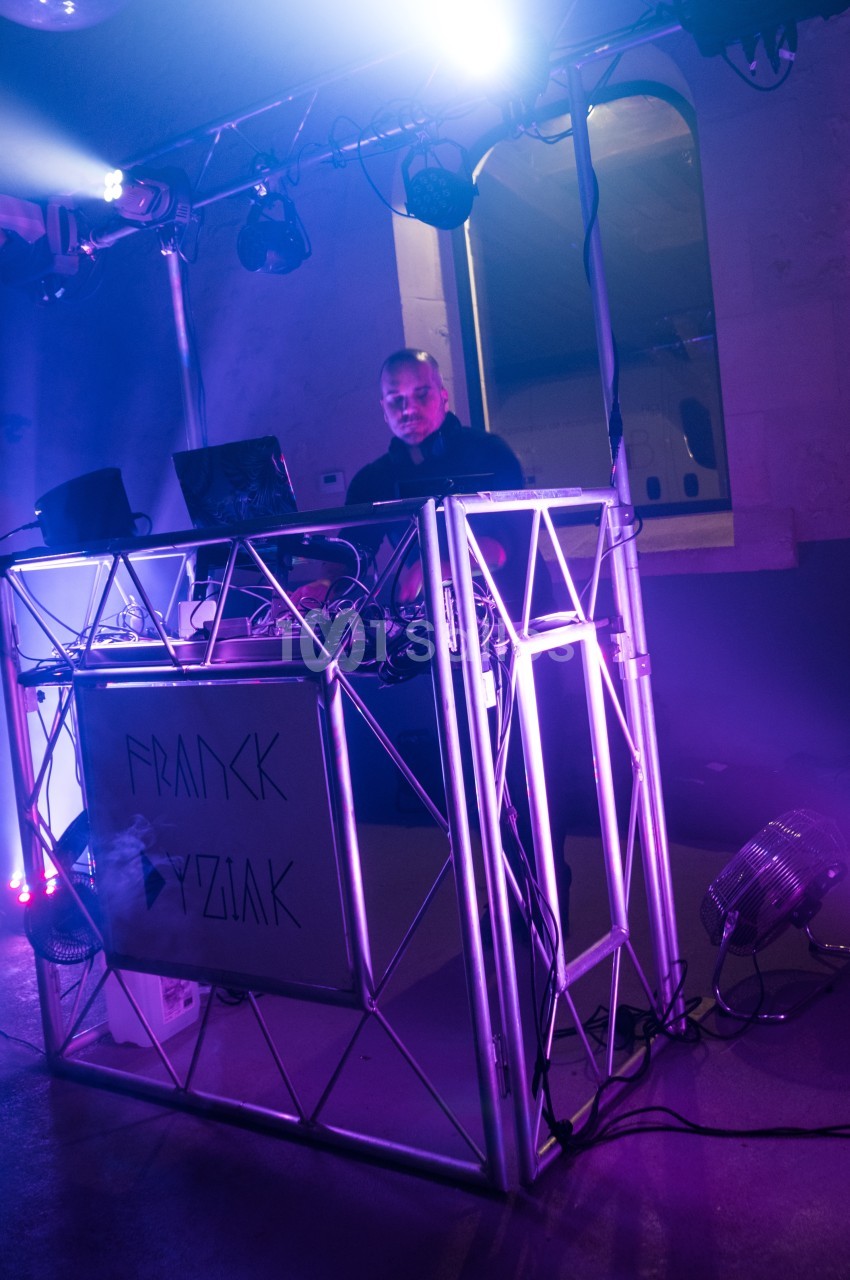 Un DJ mixant de la musique derrière une console éclairée par des lumières violettes dans une ambiance nocturne.