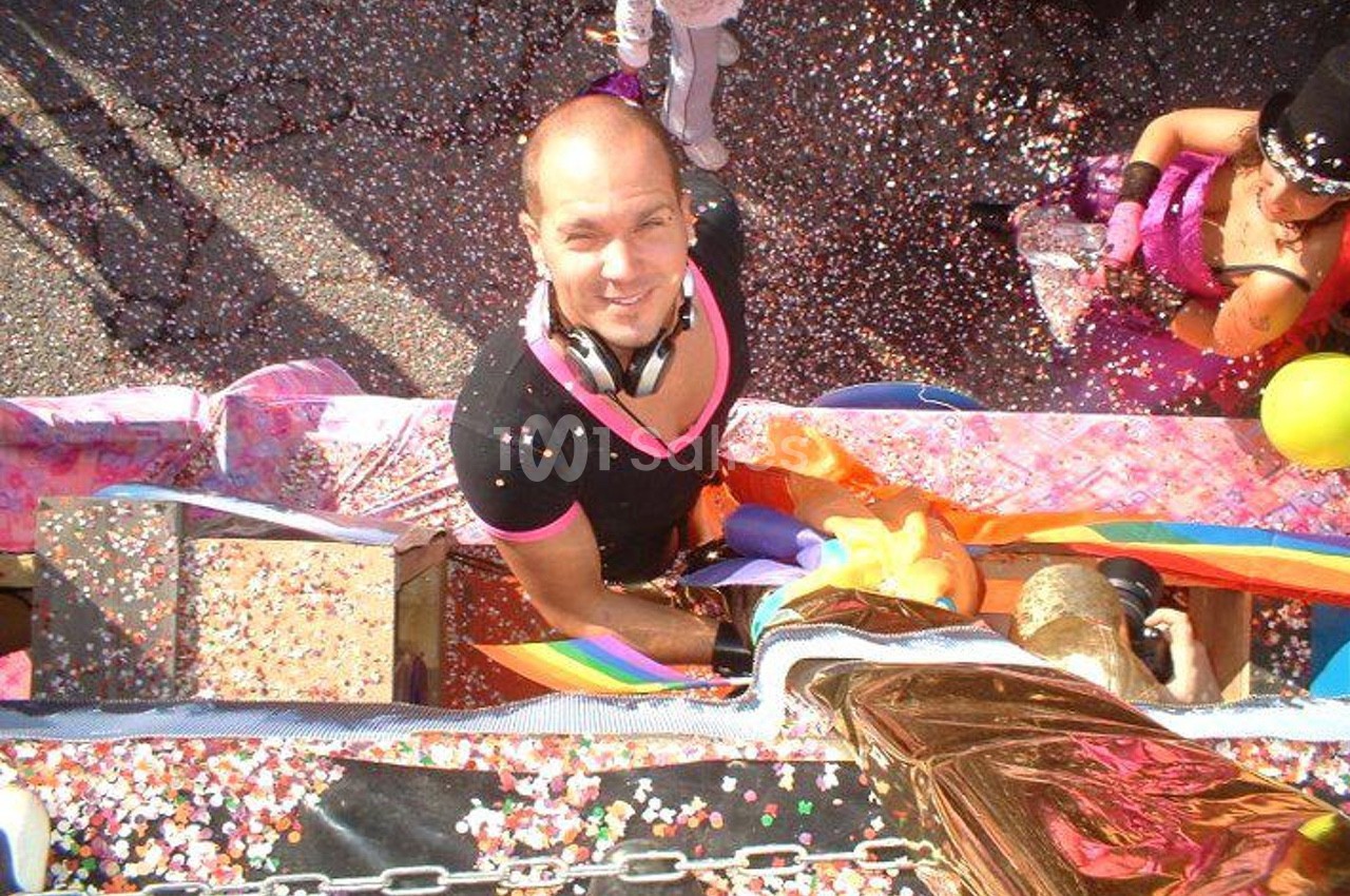 Homme souriant sur un char décoré, entouré de confettis colorés lors d'une parade festive.