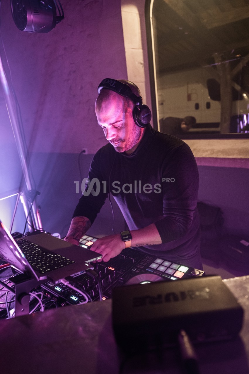 Un DJ mixant de la musique sur une console avec un ordinateur portable dans un environnement éclairé par des lumières…