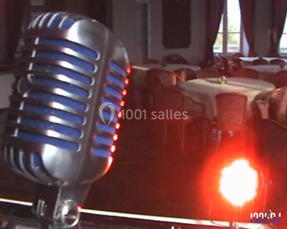 Microphone rétro en gros plan devant une salle de réception vide avec des tables et des chaises, éclairée par une lumière…