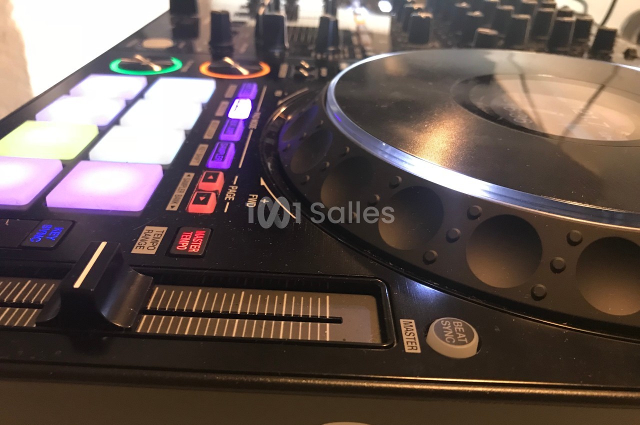 Table de mixage DJ avec platine, boutons lumineux et curseurs, utilisée pour le mixage audio.