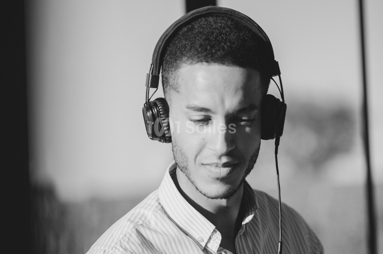 Homme portant un casque audio, regardant vers le bas dans un environnement lumineux en noir et blanc.