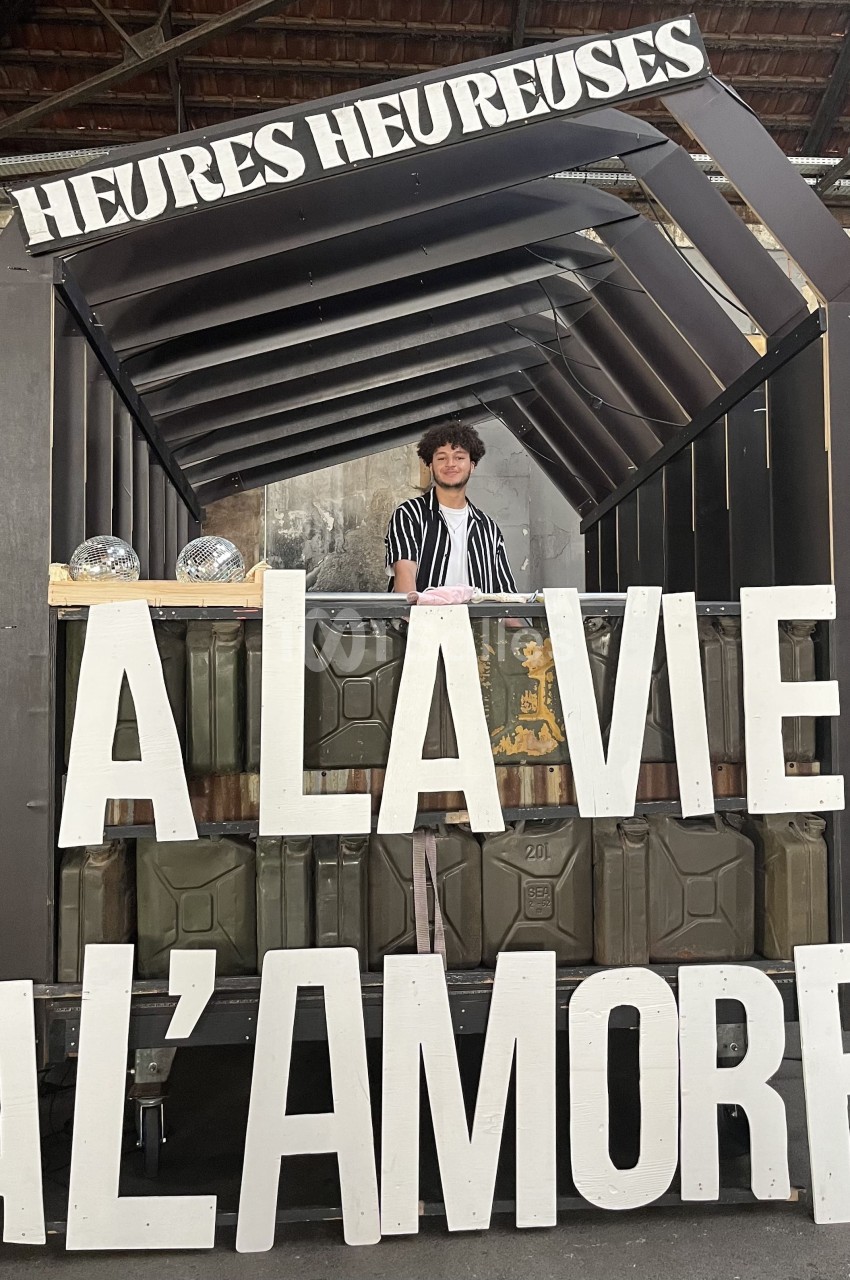 Stand décoratif avec une personne souriante derrière un comptoir, affichant les mots ’À la vie, à l'amore’.