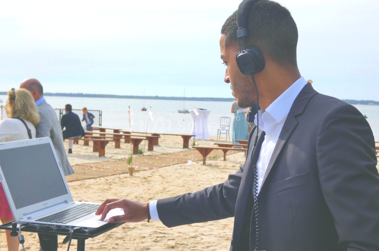 Un homme en costume utilise un ordinateur portable sur une plage, portant un casque audio.