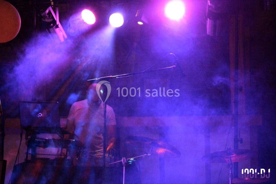 Un musicien joue sur scène dans une ambiance lumineuse violette et enfumée, entouré d'équipements.