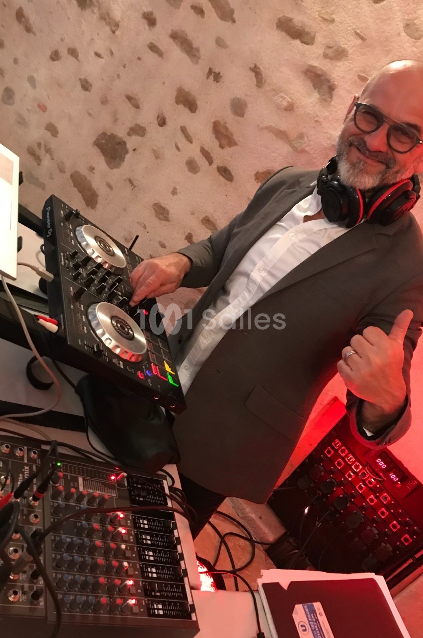 Un homme souriant en costume mixe de la musique sur une table de mixage dans un espace intérieur en pierre.