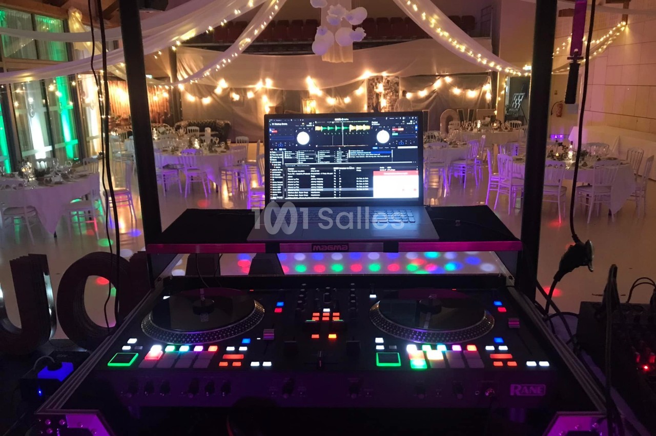 Poste de DJ avec platines lumineuses et ordinateur portable, installé dans une salle de réception décorée de guirlandes…