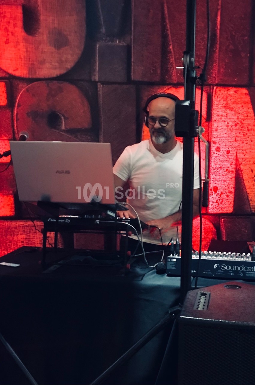 Un homme avec un casque audio mixe de la musique sur un ordinateur portable devant un mur rouge texturé.