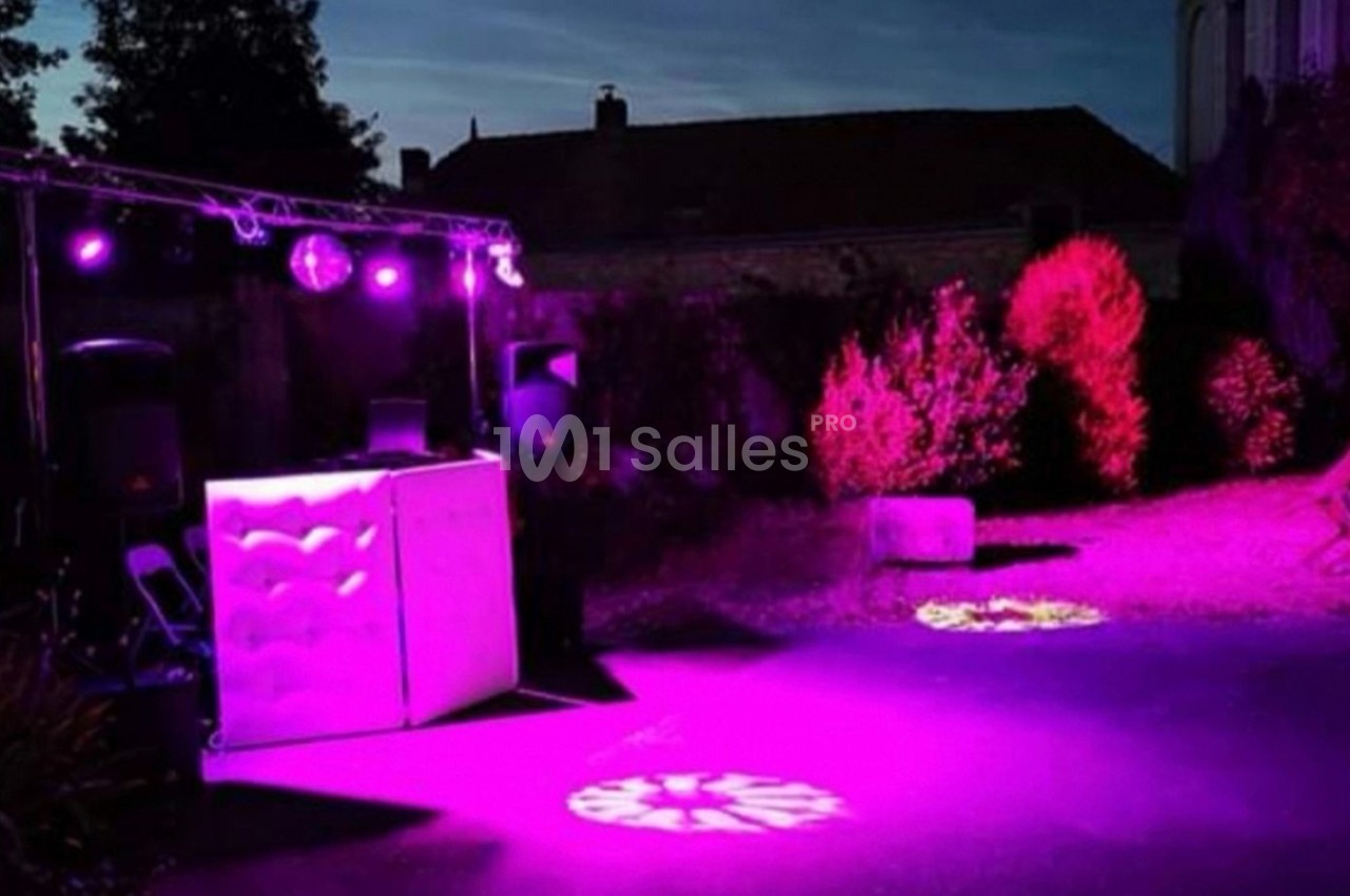Installation de DJ en extérieur avec éclairage violet et projecteurs lumineux, dans un jardin au crépuscule.
