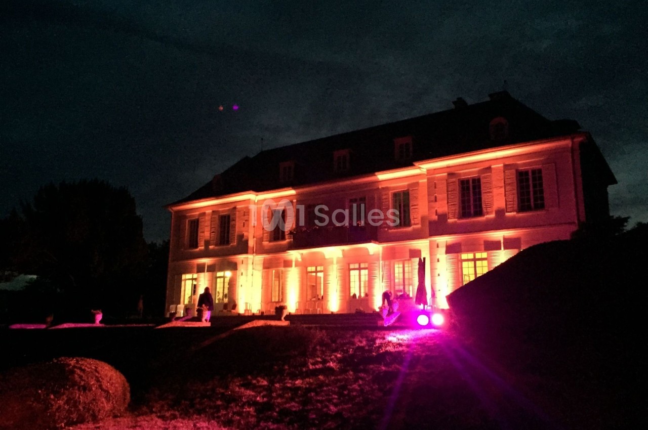 Façade d'un grand bâtiment éclairé par des lumières rouges et oranges dans un environnement nocturne.