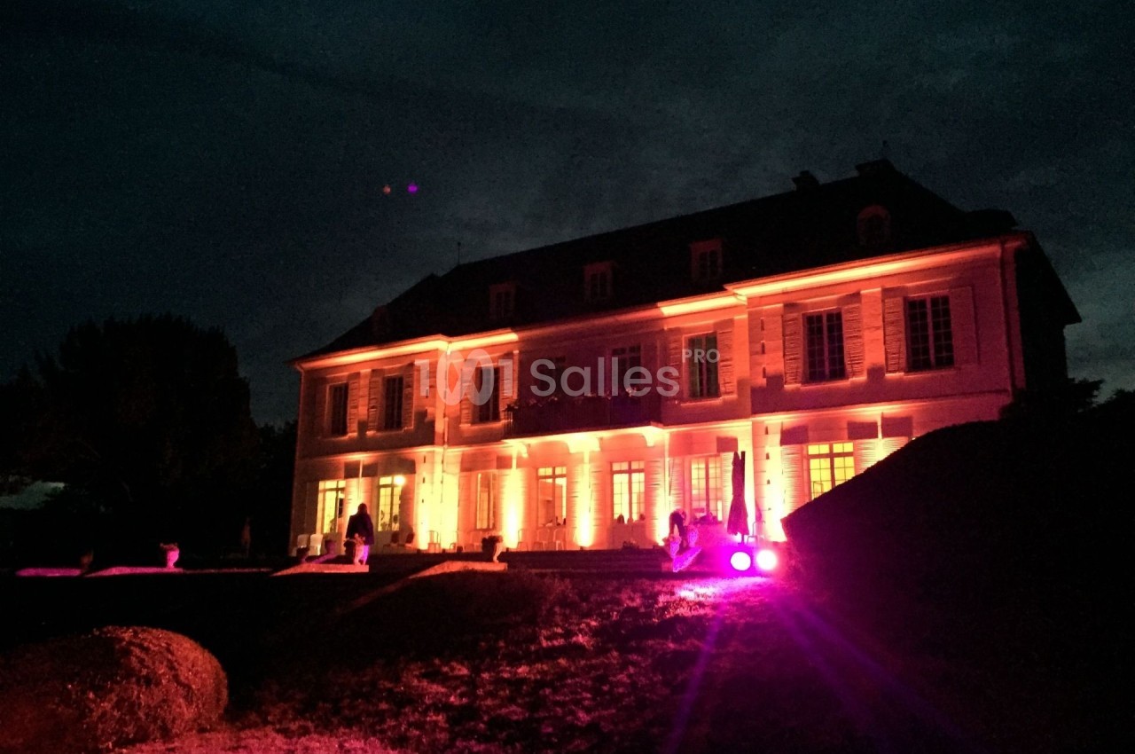 Façade d'un grand bâtiment éclairé par des lumières rouges et oranges dans un environnement nocturne.
