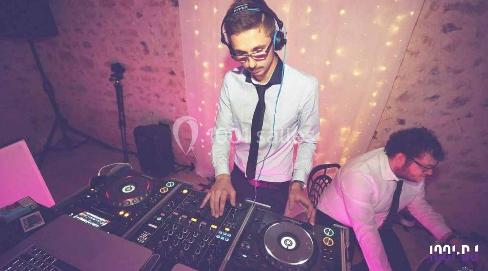 Un DJ mixe de la musique sur une table de mixage, avec un éclairage tamisé et un mur en pierre en arrière-plan.