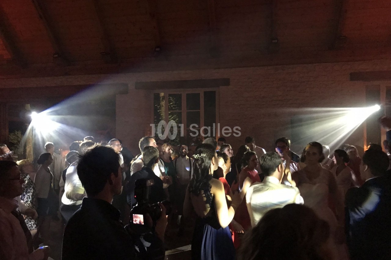 Des personnes dansent dans une salle faiblement éclairée avec des jeux de lumière et un photographe au premier plan.