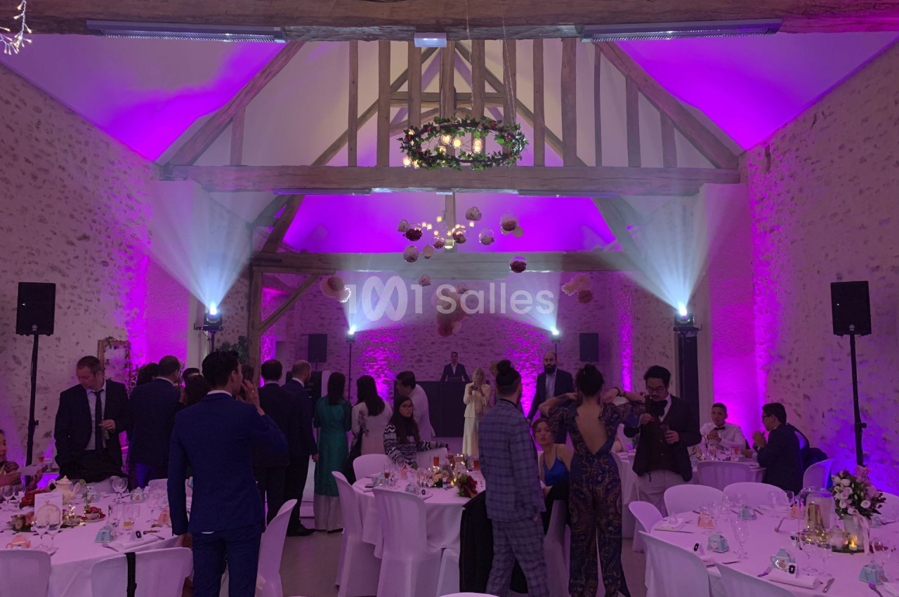 Salle de réception décorée avec des lumières violettes, des invités debout et assis autour de tables dressées.