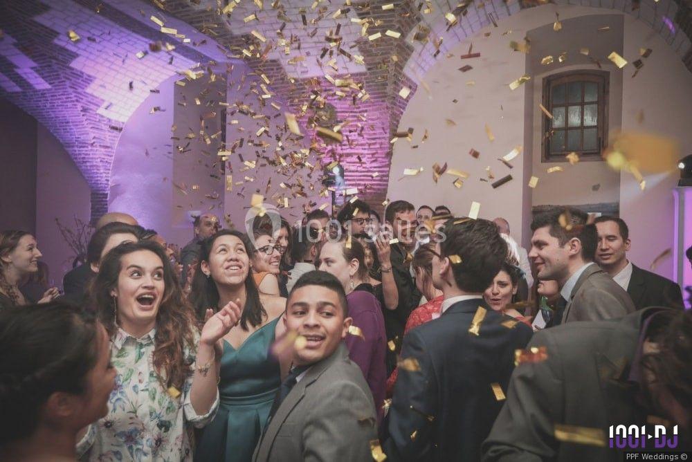 Groupe de personnes souriantes dans une salle festive, entourées de confettis dorés en plein vol.