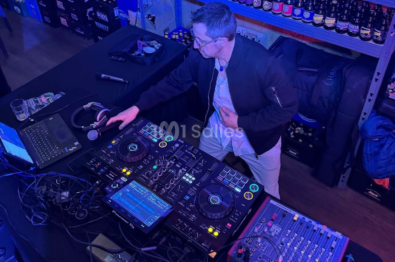 Un DJ mixe de la musique sur une console dans un environnement éclairé par des lumières bleues, entouré d'équipements.