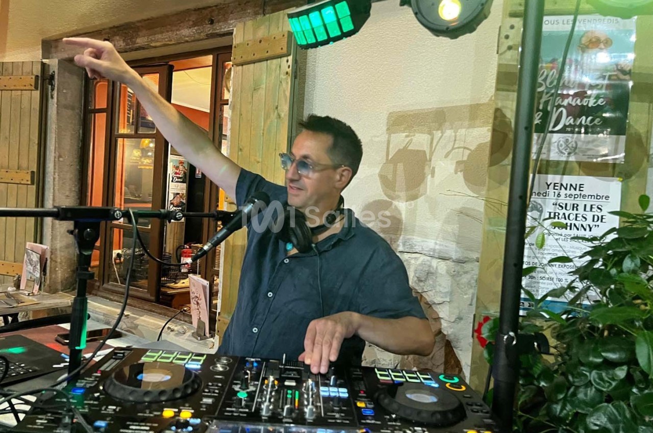 Un DJ mixe de la musique en extérieur, portant un casque autour du cou et pointant du doigt vers le public.