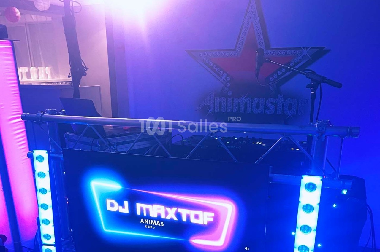 Poste de DJ avec écran lumineux affichant ’DJ MAXTOF’, éclairages colorés et décor en arrière-plan.