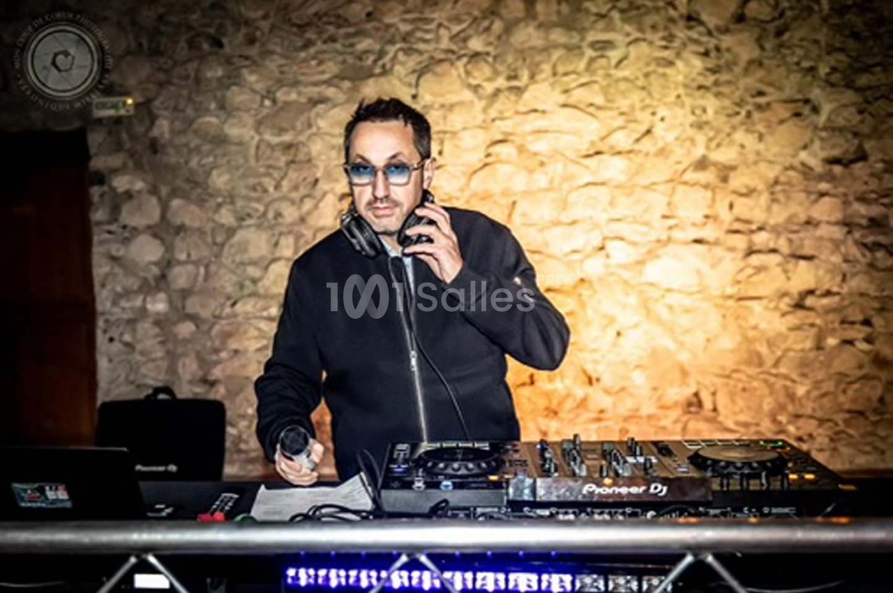 Un DJ mixant de la musique sur une table de mixage dans une salle avec un mur en pierre en arrière-plan.