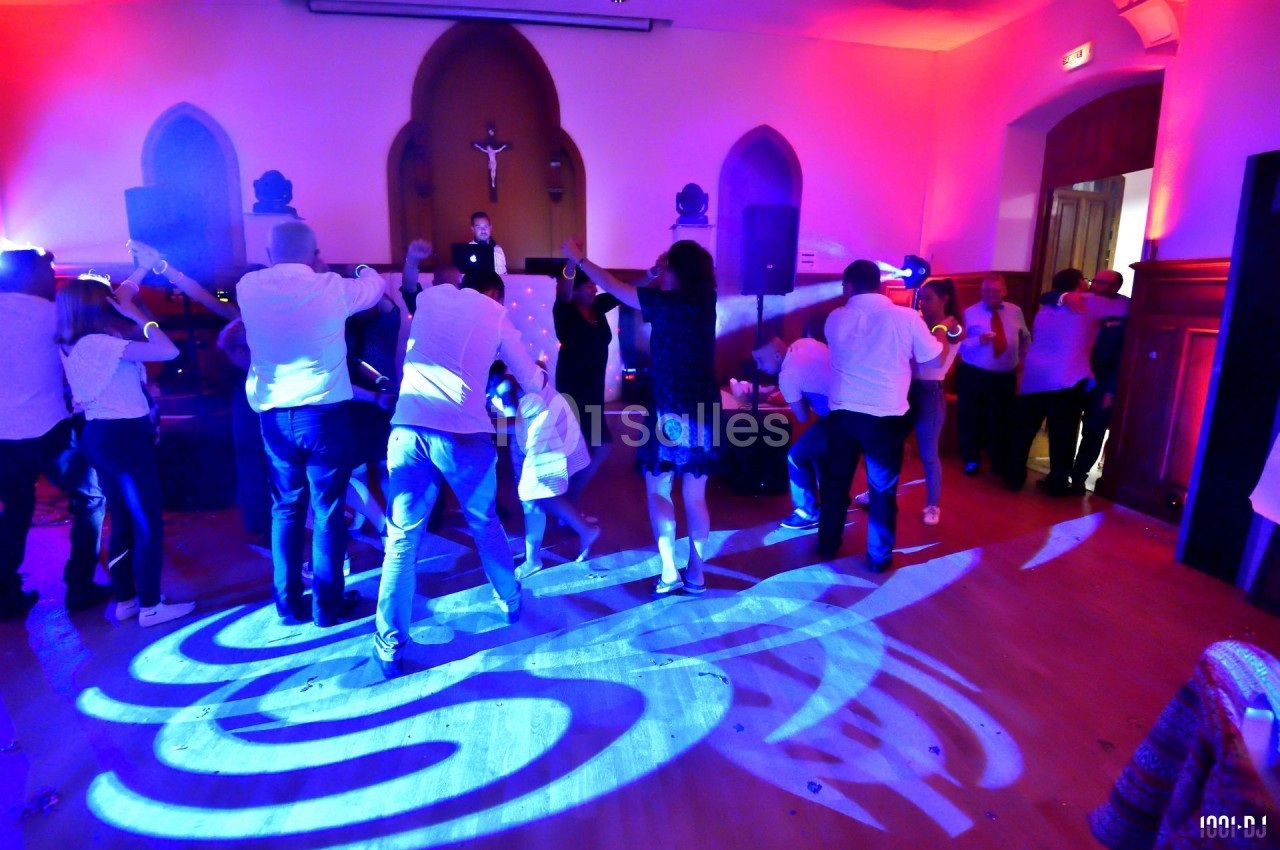 Des personnes dansent sur une piste éclairée par des lumières colorées dans une salle avec une ambiance festive.