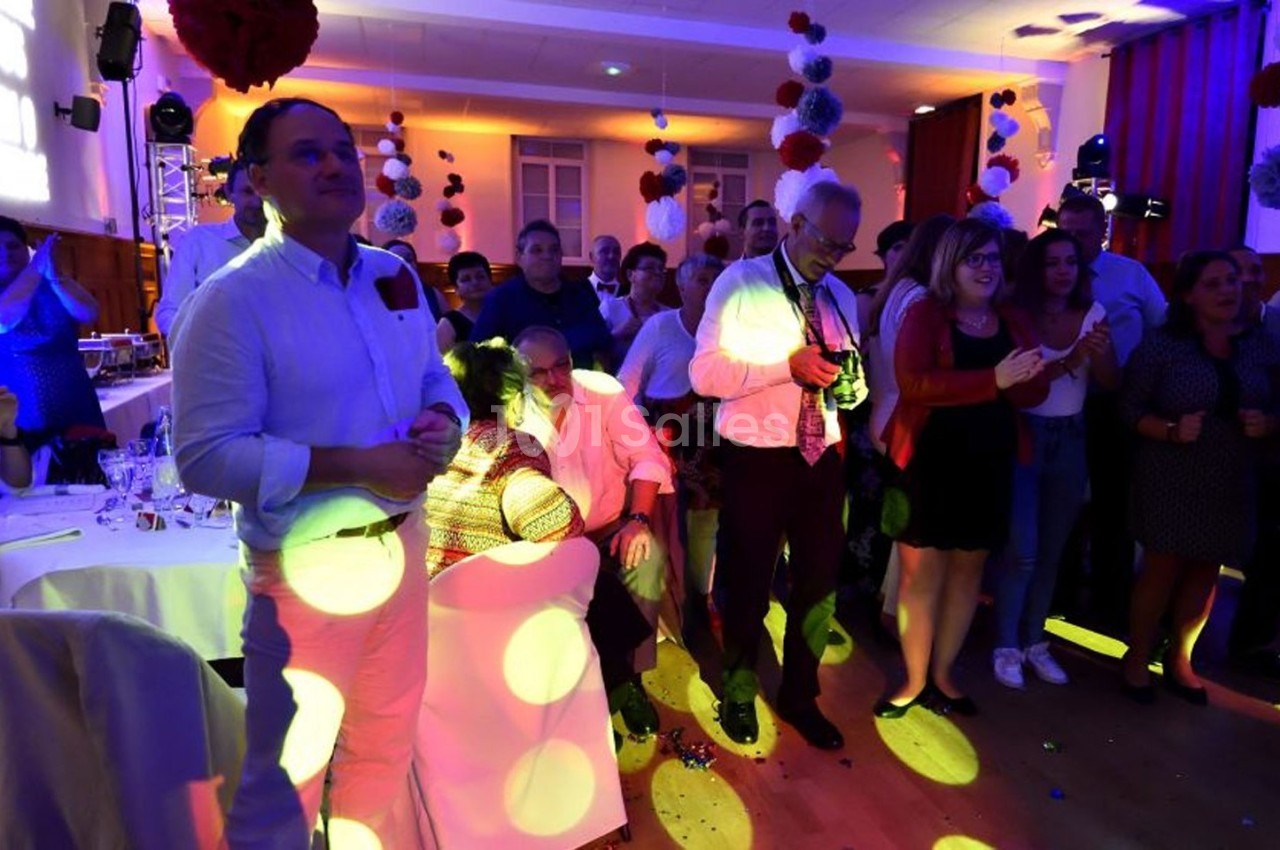 Des personnes rassemblées dans une salle décorée, éclairées par des lumières colorées lors d'un événement festif.