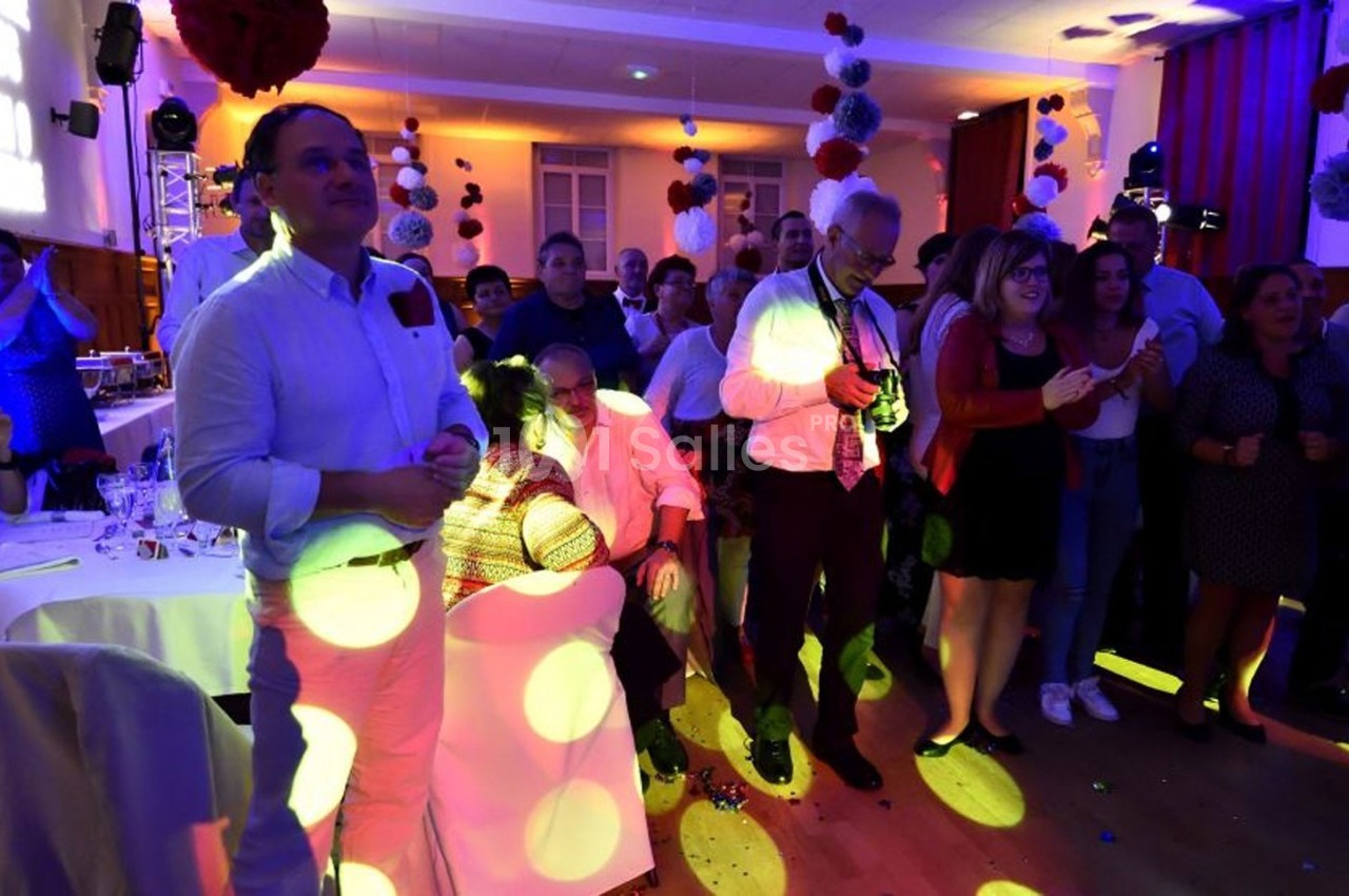 Groupe de personnes debout et assises dans une salle éclairée par des lumières colorées lors d'un événement festif.
