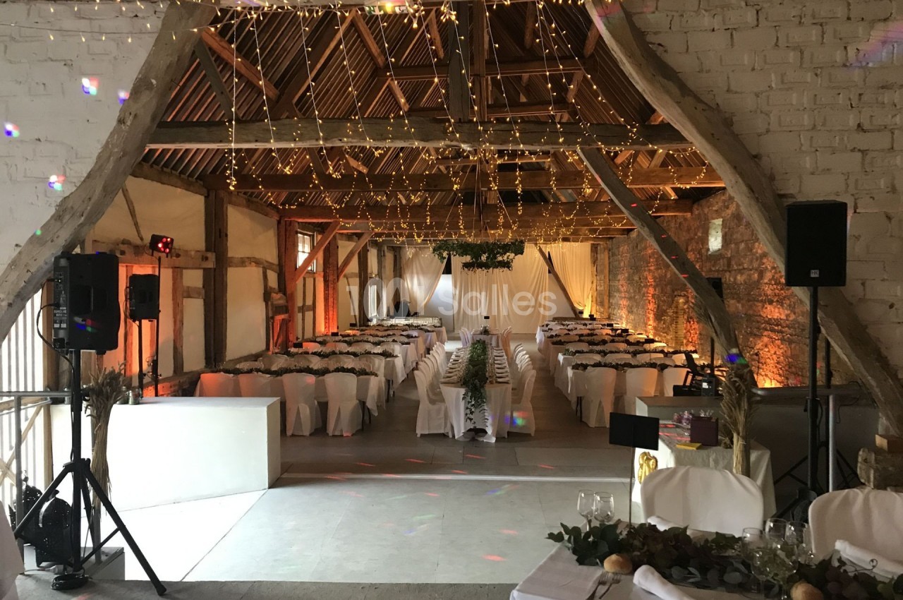 Salle de réception décorée avec des guirlandes lumineuses, des tables dressées et une ambiance chaleureuse dans une grange…
