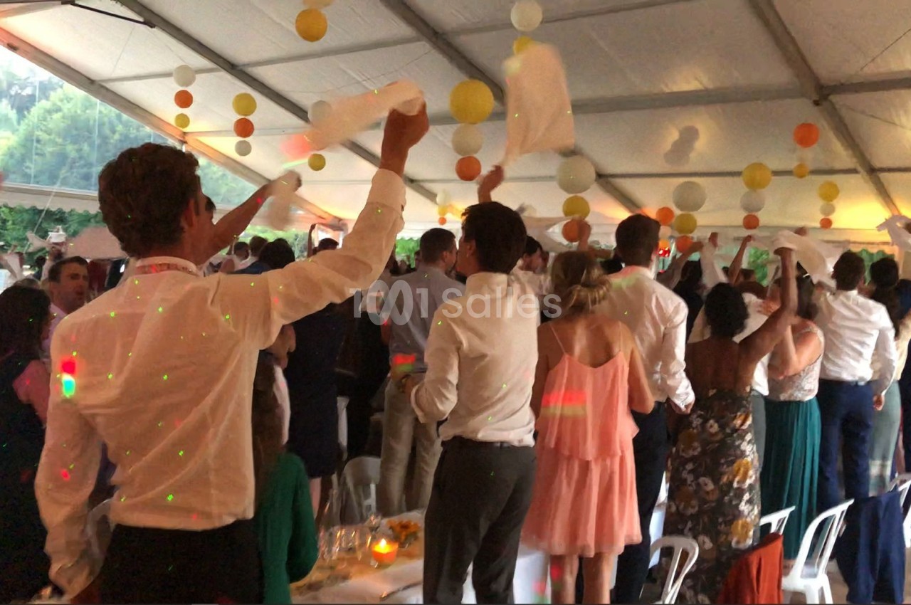 Des invités debout sous une tente festive agitent des serviettes blanches lors d'un événement convivial.