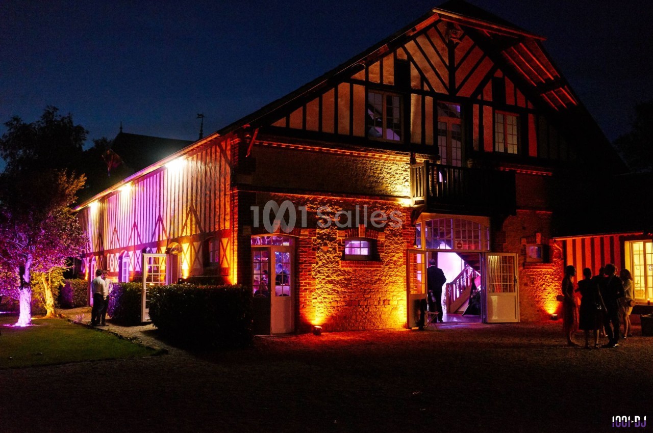 Façade d'une grande maison à colombages éclairée par des lumières colorées en soirée, avec quelques personnes à l'extérieur.