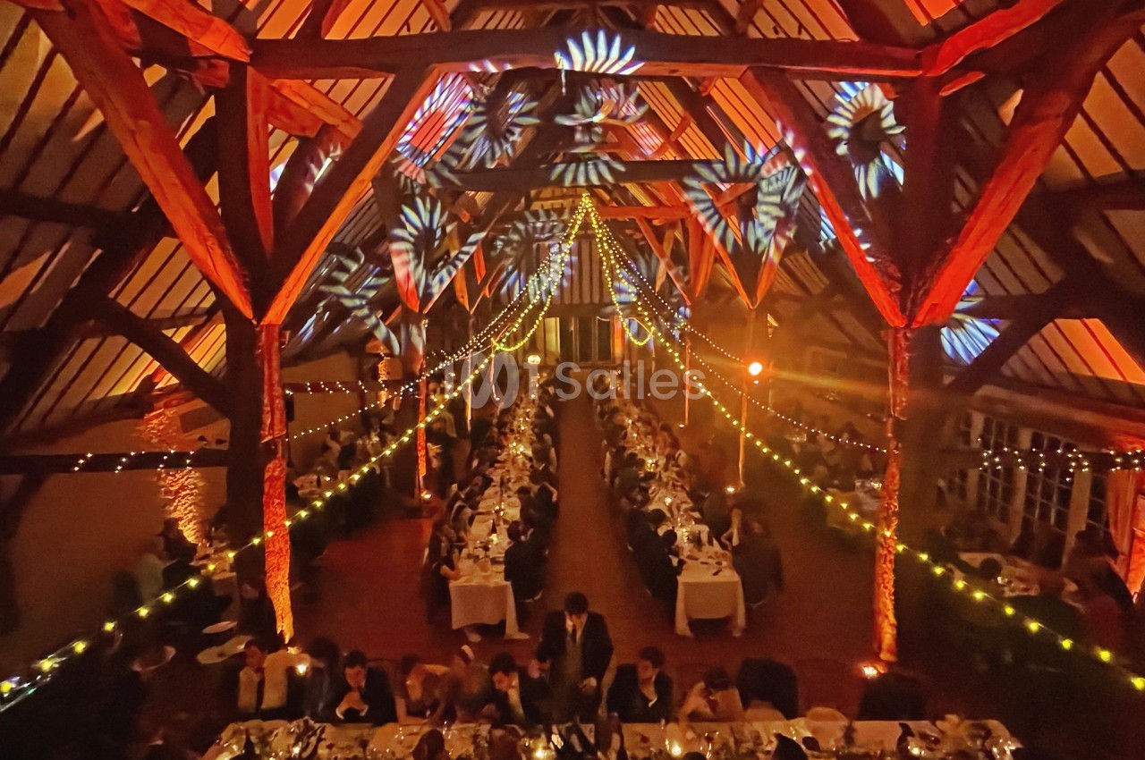 Grande salle de réception illuminée, décorée de guirlandes lumineuses et de projections colorées, avec des invités attablés.