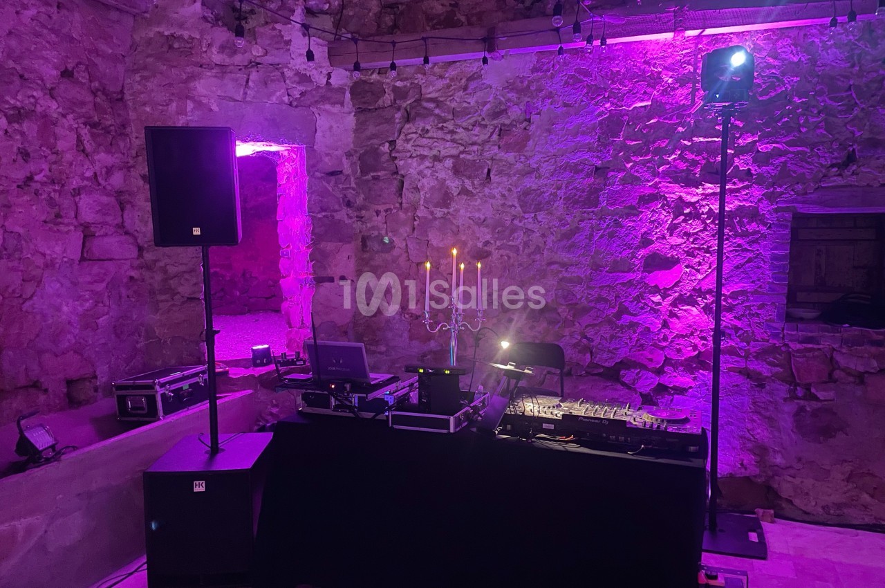 Installation de matériel de DJ avec table de mixage et éclairage violet dans une salle en pierre.